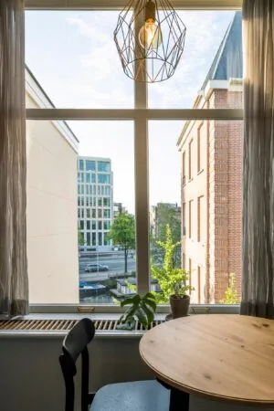 Uitzicht vanuit een appartement aan de Prof. Tulpstraat op stadsgebouwen, een straat en een gracht, met een ronde houten tafel en kamerplanten op de voorgrond.
